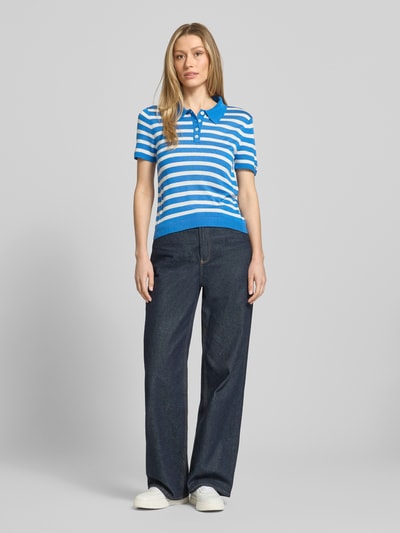 Vrouwenmodel draagt Regular Fit Poloshirt aus Lyocell-Seiden-Mix van Tommy Hilfiger met all-over patroon, logo-stiksels, polokraag, korte knoopsluiting, korte mouwen met geribde zoom, fijngebreid, blauwe en witte strepen, ganzekörperaanzicht van voren.