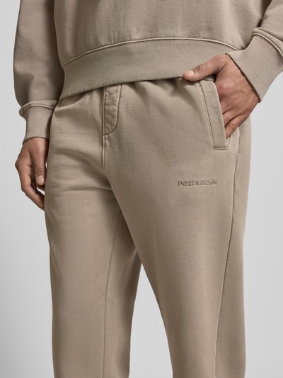 Männermodel trägt Sweatpants mit elastischem Bund van Pegador in beige, katoenmix, losse pasvorm, detailopname voorkant, Franse steekzakken, label-stitching.