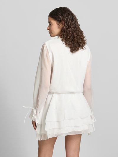 Vrouwenmodel draagt Minikleid met Rüschen und V-Ausschnitt van Gina Tricot in gebroken wit, getailleerd model met transparante mouwen, ruglengte maat XS 85 cm, borstwijdte maat XS 49 cm, mouwlengte maat XS 64 cm, geheel van achteren bekeken, Ganzkörperansicht Rückansicht.