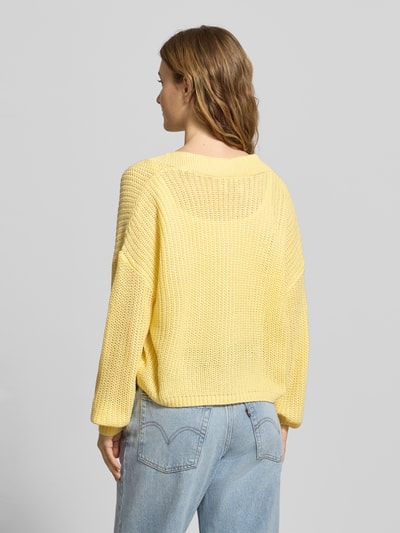 Frauenmodel trägt Regular Fit Strickjacke mit einreihiger Knopfleiste Modell 'CAROL NICE' von Only in Gelb, Strickoptik, Ganzkörperansicht Rückansicht.