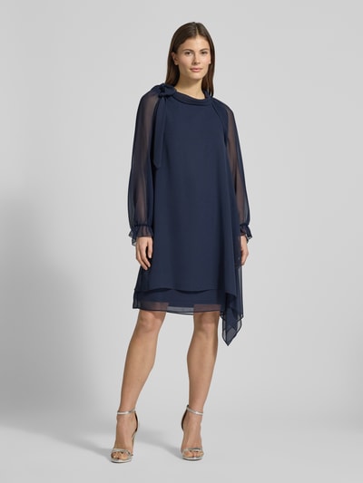 Frauenmodel trägt Relaxed Fit Bolero in semitransparentem Design von V.M., dunkelblau, leichte Rüschenbesatz an elastischen Ärmelabschlüssen, Langarm, Rückenlänge 41 cm bei Größe 36, Semitransparenz, Ganzkörperansicht von vorne.