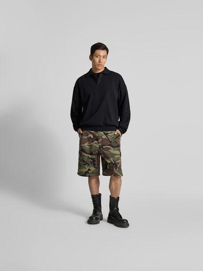 Männermodel trägt Regular Fit Poloshirt aus Baumwoll-Mix von VETEMENTS in Schwarz, Polokragen, Relaxed Fit, Ganzkörperansicht von vorne.