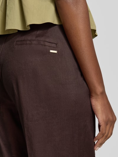 Frauenmodel trägt Hose aus Leinen-Mix mit Bügelfalten Modell 'CARLA' von Guess in Dunkelbraun, glatte Struktur, Nahaufnahme Hüfte von hinten, Damen Hose von Guess, Regular Fit, Lyocell-Anteil.