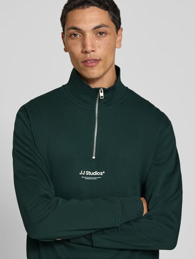Männermodel trägt Regular Fit Sweatshirt aus Baumwoll-Mix Modell 'Soho' von JACK & JONES, dunkelgrün mit Logo-Print, Nahaufnahme Oberkörper