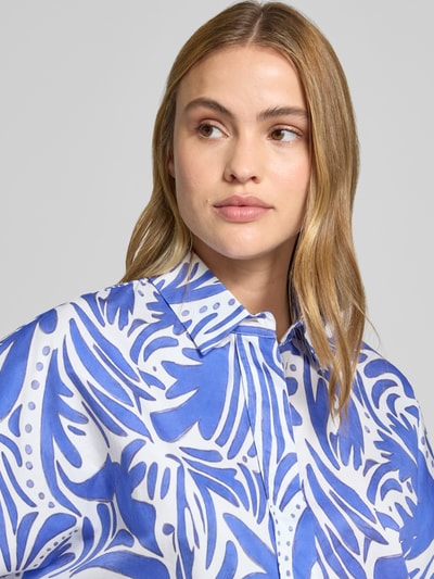 Frauenmodel trägt Bluse mit verdeckter Knopfleiste und 3/4-Arm von Christian Berg Woman aus reiner Baumwolle, Regular-Fit, Hemdblusenkragen, abstraktes blau-weißes Muster, Nahaufnahme Oberkörper.