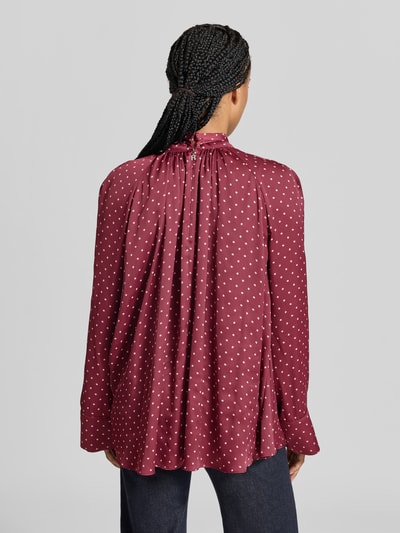 Vrouwenmodel draagt Regular Fit Bluse aus Satin van ROTATE met opstaande kraag, sierstrik, lange mouwen, ruglengte maat 36: 70 cm, mouwlengte maat 36: 63 cm, wijnrode kleur met witte stippen, soepel vallende satijnstructuur, volledig zicht op de rug, KI-modified