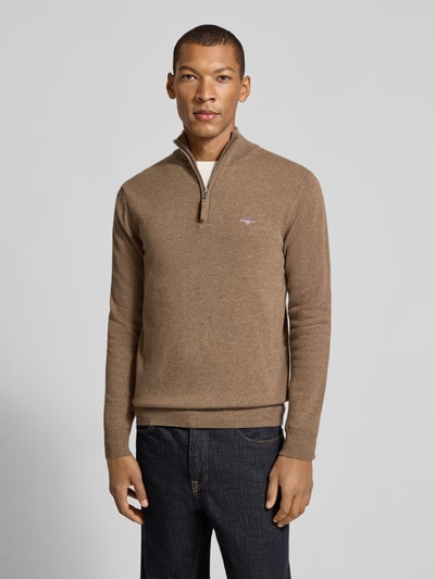 Männermodel trägt Pullover aus reiner Wolle von GANT in Braun, Feinstrick mit Reißverschluss und hohem Kragen, Ganzkörperansicht von vorne.