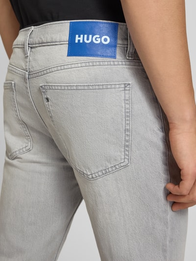 Männermodel trägt Tapered Straight Fit Jeans aus Baumwoll-Mix Modell 'BRODY' von HUGO Blue, hellgrauer Denim mit Label Patch, Nahaufnahme Rückansicht.