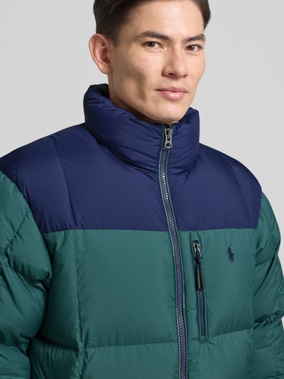 Męskim model nosi Kurtka puchowa z zamkiem błyskawicznym dwustronnym i stójką od Polo Ralph Lauren, wypełnienie puchem i pierzem, krój regular fit, wyhaftowane logo, kieszeń na piersi, kolor zielony z granatem, widoczna faktura materiału, nahaufnahme oberkörper. Długość tyłu 73 cm, szerokość ramion 50 cm, szerokość klatki piersiowej 57 cm, długość rękawów 70 cm dla rozmiaru M.