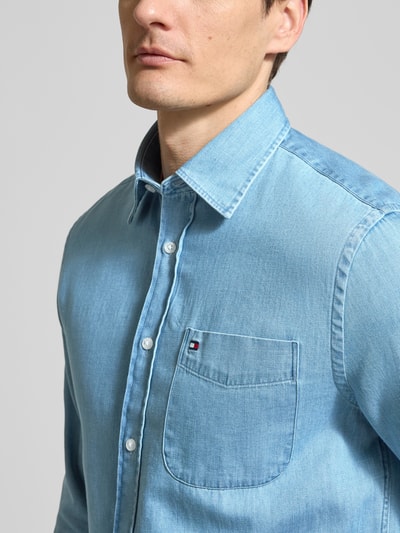 Männermodel trägt Regular Fit Jeanshemd aus reiner Baumwolle von Tommy Hilfiger in Denim-Optik mit Haifischkragen, Nahaufnahme Oberkörper.