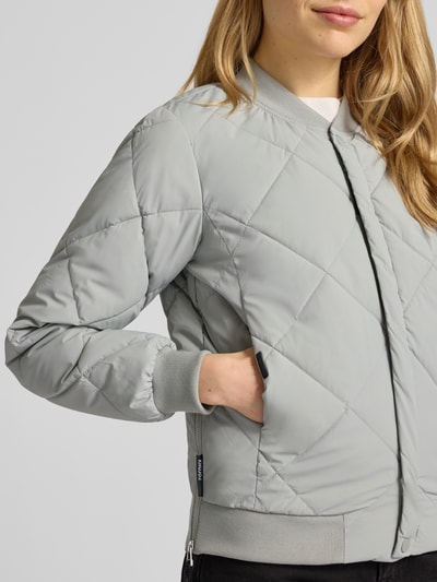 Kobiece model prezentuje Steppjacke mit Knopfleiste Modell 'ANGE2' od khujo, jasnoszara, krój regular fit, z kołnierzem stójką, z przeszyciami, szerokość w rozmiarze S: 46 cm, długość tyłu: 59 cm, długość rękawa: 61 cm, szerokość ramion: 36 cm, zapięcie na guziki, tekstura pikowana. Zbliżenie na górną część ciała z przodu.