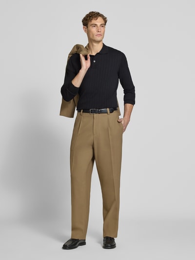 Männermodel trägt Regular Fit Poloshirt aus reiner Baumwolle Modell 'TORINO' von Selected in Schwarz, kombiniert mit beigen Hosen, Ganzkörperansicht von vorne.