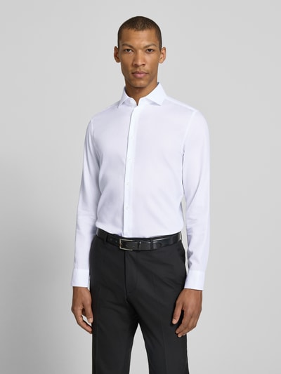 Männermodel trägt Slim Fit Business-Hemd aus Baumwolle mit Kentkragen von SEIDENSTICKER, weiß, feine Struktur, Knopfleiste, Ganzkörperansicht von vorne.