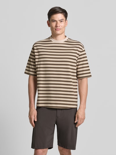 Męski model nosi Relaxed Fit T-Shirt aus reiner Baumwolle Modell 'ASPEN 2' od SELECTED HOMME w beżowo-brązowe paski, tekstura miękka, Ganzkörperansicht von vorne.