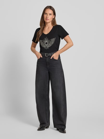 Frauenmodel trägt T-Shirt mit Label-Detail Modell 'Gethi' von MOS MOSH aus reiner Baumwolle, Regular Fit, U-Ausschnitt, schwarze Farbe, Ganzkörperansicht von vorne.