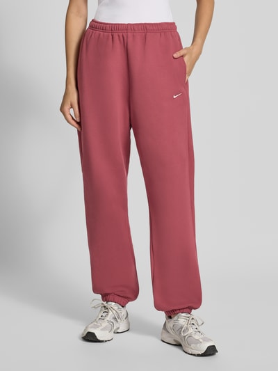 Frauenmodel trägt Oversized Sweathose aus Baumwoll-Mix von Nike in Altrosa, glatte Struktur, Ganzkörperansicht von vorne, Damen Sweathose von Nike.
