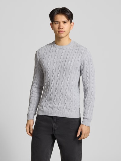 Męski model nosi Strickpullover mit Zopfmuster und Logo-Stitching od REVIEW, jasnoszary, bawełniany, krój modern fit, prążkowane wykończenia, widoczny wzór warkocza, okrągły dekolt, długość tyłu 70 cm, długość rękawa 74 cm, całkowity widok z przodu.