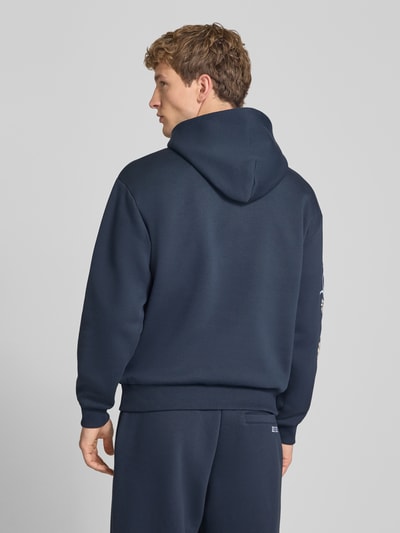 Männermodel trägt Relaxed Fit Hoodie mit Känguru-Tasche von REVIEW in Dunkelblau, florale Stickerei, Rückenansicht, Baumwoll-Mix.