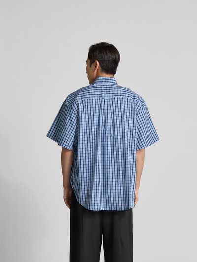 Männermodel trägt Oversized Freizeithemd mit Brusttasche von VETEMENTS in Blau mit Karomuster, Reine Baumwolle, Oversized-Fit, Kurzärmelig, Kentkragen, Rückenlänge bei Größe M 82 cm, Schulterbreite 55 cm, Ärmellänge 29 cm, Ganzkörperansicht Rückansicht.