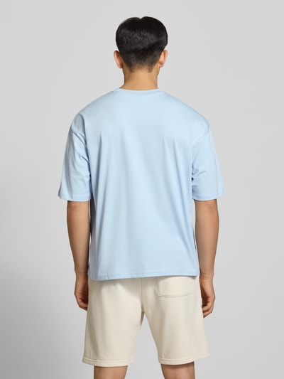 Męski model nosi T-Shirt mit Logo- und Motiv-Print od REVIEW, jasnoniebieski kolor, bawełna, krój loose fit, widok całej sylwetki z tyłu