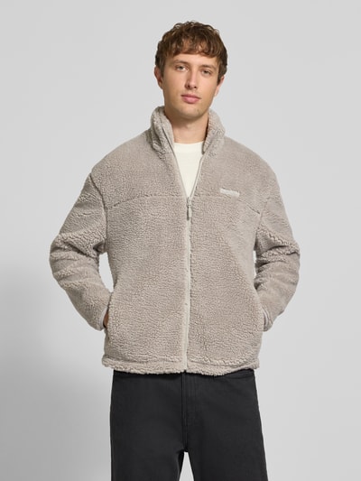 Männermodel trägt Fleecejacke mit Label-Detail und Reißverschluss von REVIEW, beige, Teddyfell-Optik, Regular Fit, Ganzkörperansicht von vorne.