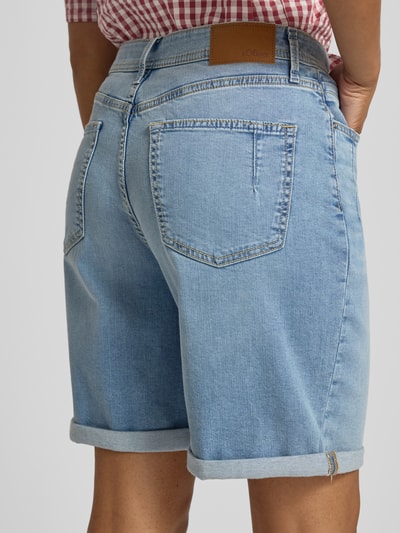 Vrouwenmodel draagt Regular Fit Jeansshorts uit katoenmix model 'SURI' van s.Oliver RED LABEL, lichtblauw denim met omslag, vijfzakken-design, nieten, label patch, riemlussen, knoop- en ritssluiting, detailopname achteraan.