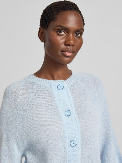 Frauenmodel trägt Wolljacke mit Mohair-Anteil von Marc Cain, hellblauer Material-Mix mit Rundhalsausschnitt und Knopfleiste, Nahaufnahme Oberkörper.