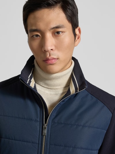 Männermodel trägt Jacke mit Stehkragen von Christian Berg Men in Dunkelblau, Regular-Fit, Nahaufnahme Oberkörper, Reißverschluss, Reißverschlusstaschen, gerippte Abschlüsse, Rückenlänge bei Größe M 26 cm, Schulterbreite 19 cm, Brustweite 19 cm, Ärmellänge 26 cm.
