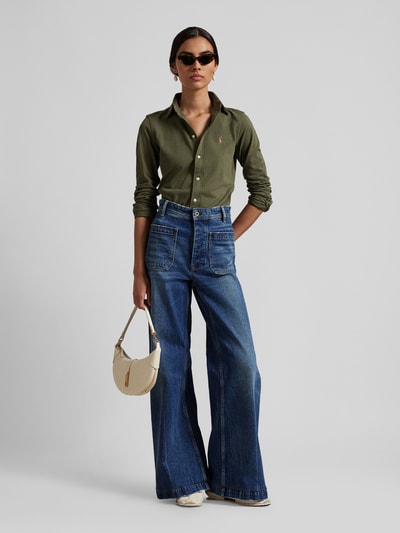 Frauenmodel trägt Hemdbluse mit Label-Stitching von Polo Ralph Lauren aus reiner Baumwolle, Slim Fit, Button-Down-Kragen, olivgrün, kombiniert mit blauer Schlagjeans und cremefarbener Tasche, Ganzkörperansicht von vorne.