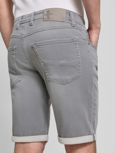 Männermodel trägt Bermudas in Denim-Optik mit Eingrifftaschen von MAC, grauer Baumwoll-Elasthan-Mix, Used-Look, Umschlag, Ganzkörperansicht Rückansicht.