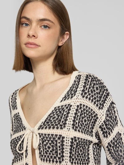 Kobiece modelka nosi Regular Fit Strickjacke aus Baumwoll-Mix Modell 'LOA' od Only w dwukolorowej czerni i kremowym, krój regular fit, dzianinowa faktura, z wiązaniem z przodu, dekolt w serek, długi rękaw, zbliżenie na górną część ciała