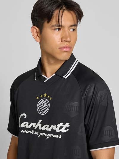 Männermodel trägt schwarzes Funktionsshirt mit weißem Logo und Rundhalsausschnitt von Adidas, Modell 'Terrace', Nahaufnahme Oberkörper. Herren Funktionsshirt Regular Fit, Rückenlänge bei Größe M: 71 cm.