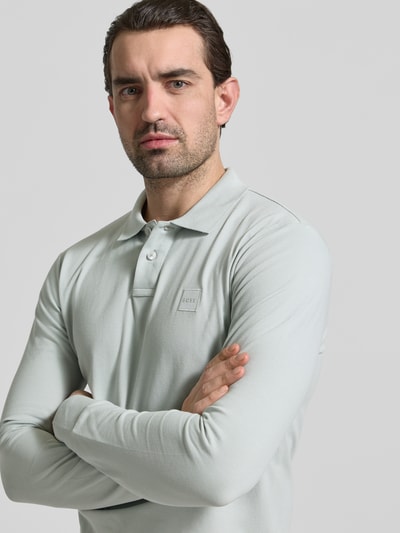 Männermodel trägt Slim Fit Poloshirt aus Baumwoll-Mix Modell 'PASSERBY' von BOSS Orange in Unifarbe, Nahaufnahme Oberkörper.