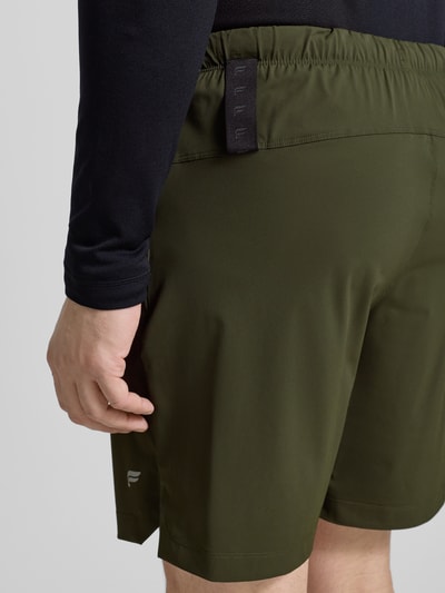 Männermodel trägt Regular Fit Shorts mit Logo-Print von Fabletics in Olivgrün, elastischer Bund, Eingrifftaschen, Ganzkörperansicht Rückansicht.