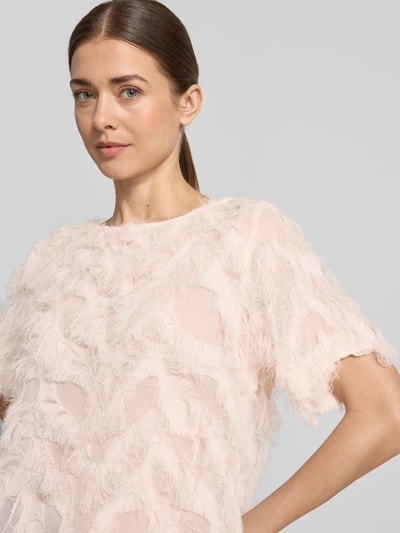 Kobiece modelka nosi Boxy Fit Blusenshirt mit Fransen-Design Modell 'MYLINE' od Selected Femme, jasnoróżowy, strukturalny, lekko przezroczysty, krótkie rękawy, dekolt typu łódka, materiał chiffon, widoczne frędzle, ujęcie: zbliżenie górnej części ciała.