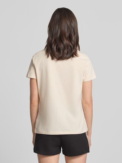 Kobiece modelka ma na sobie Regular Fit T-Shirt mit Logo-Applikation Modell 'Colette' od Guess Activewear, kremowy elastyczny bawełniany miks, slogan na plecach, okrągły dekolt, długość tyłu w rozmiarze S: 60 cm, Ganzkörperansicht Rückansicht.