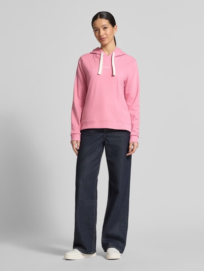 Vrouwenmodel draagt Regular Fit Hoodie aus Baumwoll-Mix van Tom Tailor Denim, roze effen sweatstof met borduursel, lange mouwen, geribde boorden, capuchon met tunnelkoord, zijsplitten, voorkant volledig zichtbaar, geheellichaamsaanzicht van voren.