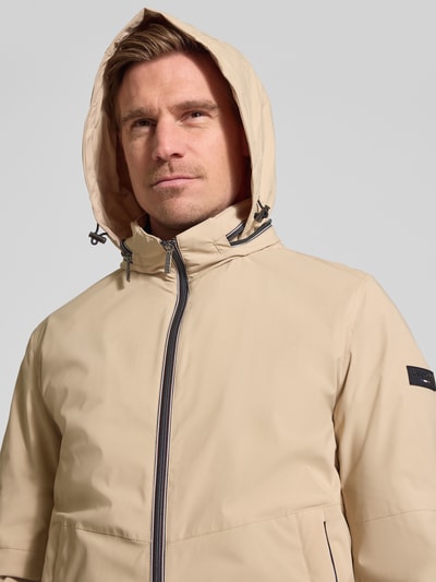 Männermodel trägt Regular Fit Jacke mit Stehkragen von bugatti in Beige mit Logo-Detail, Zweiwege-Reißverschluss, Kapuze, Nahaufnahme Oberkörper.