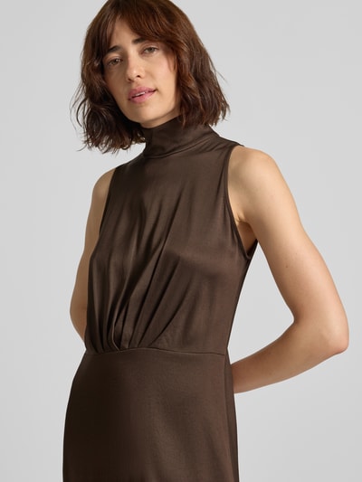 Frauenmodel trägt Maxikleid mit Stehkragen und Drapierungen Modell 'AMABEL' von DRYKORN in Braun, Material-Mix mit Stretch, Nahaufnahme Oberkörper.