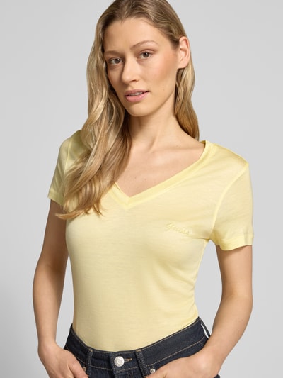 Frauenmodel trägt Slim Fit T-Shirt aus reinem Lyocell von Guess in Hellgelb mit V-Ausschnitt und Logo-Stitching, Nahaufnahme Oberkörper.
