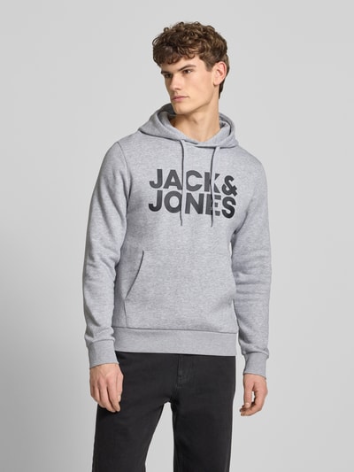 Męski model nosi Hoodie z nadrukiem labelu i kieszenią kangurką od Jack & Jones, bawełniany miks, regular fit, jasnoszary kolor, widok na całe ciało z przodu.