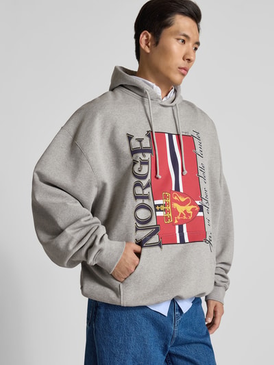 Männermodel trägt Oversized Hoodie mit Motiv-Print von VETEMENTS in Grau, Känguru-Tasche, Kapuze, Baumwoll-Mix, Ganzkörperansicht von vorne.