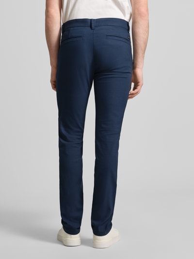 Męski model nosi Slim Fit Chino aus Baumwoll-Mix mit Leinen und Viskose-Anteil Modell 'Chino-Slim-2' von BOSS Orange, tkanina stylizowana na denim, krój slim fit, średni stan, naszywka z logo, wpuszczane kieszenie, kieszeń z tyłu, splot twill, mieszanka bawełny, lnu i wiskozy, granatowy kolor, tekstura gładka, widok całej sylwetki z tyłu.