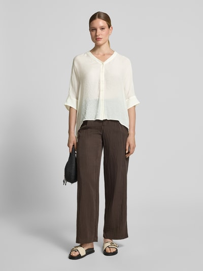 Modelka nosi Relaxed Fit Bluse aus Viskose-Mix mit 3/4-Arm od comma, kolor kremowy, guziki, brązowe spodnie, długość tyłu 62 cm, długość rękawa 18 cm, mieszanka wiskozy, dekolt w serek, listwa guzikowa, rękaw o dł. 3/4, widok całej sylwetki z przodu.