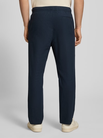 Männermodel trägt Pull On Hose in Leinen-Optik mit Eingrifftaschen von REVIEW in Dunkelblau, elastischer Bund, Gesäßleistentasche, Ganzkörperansicht Rückansicht.