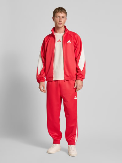Männermodel trägt T-Shirt mit Label-Print von adidas Sportswear in Weiß, lockerer Schnitt, reine Baumwolle, Ganzkörperansicht von vorne.