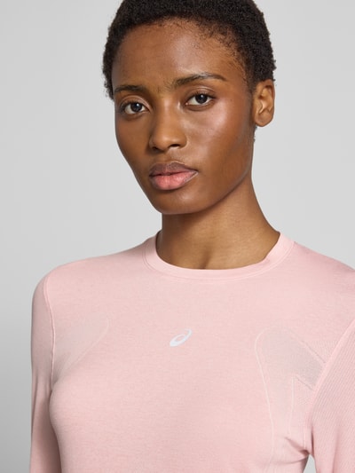 Frauenmodel trägt Slim Fit Longsleeve mit Logo-Print Modell 'Road' von ASICS TIGER in zartem Rosa, strukturierte Oberfläche, Nahaufnahme Oberkörper. Damen Longsleeve, Rundhalsausschnitt, Rückenlänge bei Größe S 61 cm.