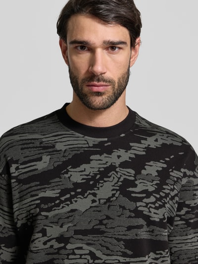 Männermodel trägt Regular Fit T-Shirt aus reiner Baumwolle Modell 'TE_WILDNATURE' von BOSS Orange mit abstraktem Allover-Muster, Nahaufnahme Oberkörper.