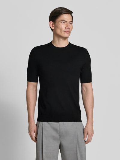 Männermodel trägt Slim Fit T-Shirt aus Strick von HUGO, schwarze Strick-Optik, Rundhals, Kurzarm, Label-Stitching-Applikation, Ganzkörperansicht von vorne.