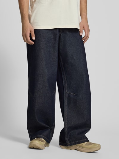 Männermodel trägt Wide Fit Jeans mit Logo-Stitching von KARL KANI, dunkles Denim, lockere Passform, 5-Pocket-Design, Ganzkörperansicht von vorne.